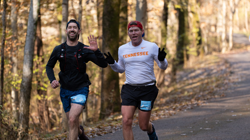 Two men running a marathon on a road in the fall