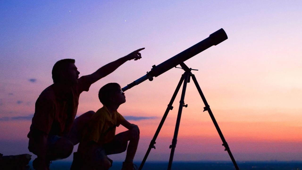 parent and child stargazing through a telescope